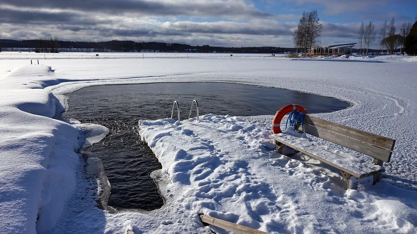 Agujero en el hielo para baño de invierno en un lago congelado en Peurunka, Finlandia, con escalera, salvavidas y banca en la nieve