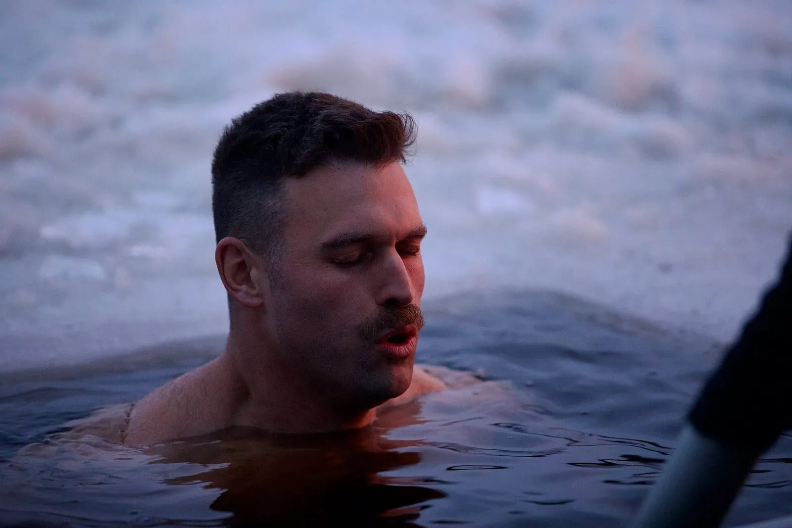 Hombre con los ojos cerrados sumergido hasta los hombros en un agujero en el hielo, durante un baño de invierno en Finlandia