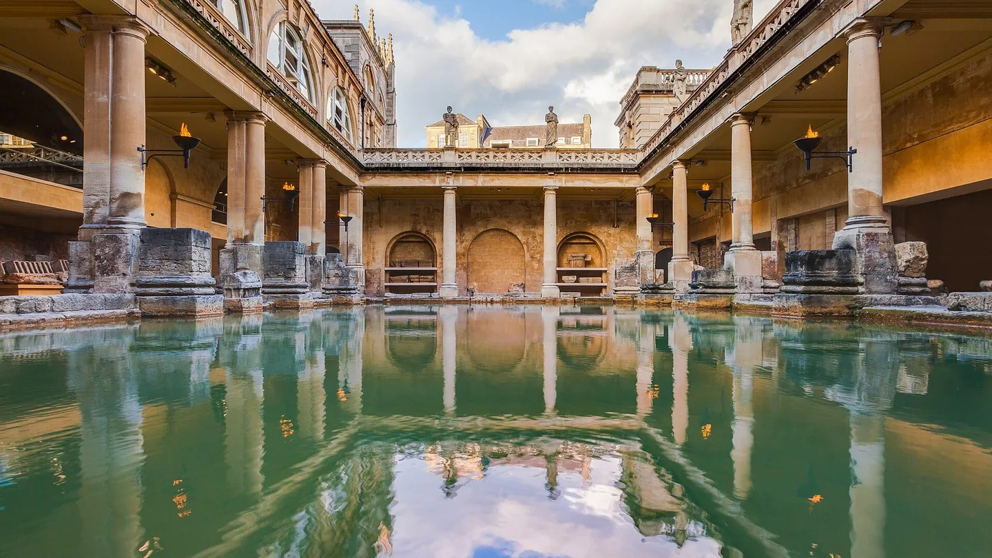 El Great Bath de las Termas Romanas de Bath, en Inglaterra, con la alberca de agua verde rodeada de columnas y el piso superior del siglo XIX