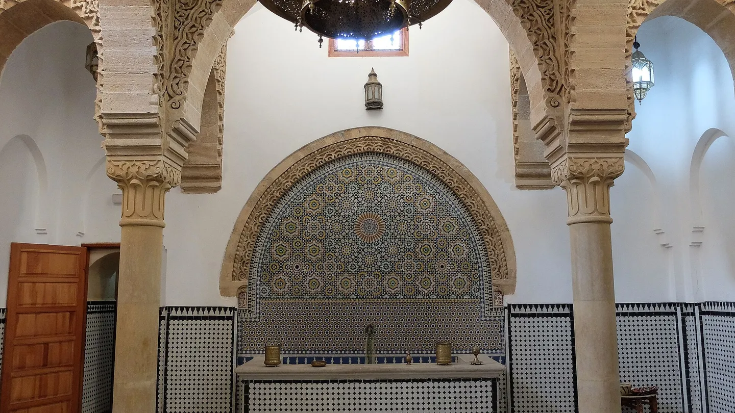 Salón de recepción del Hammam Saffarin, en Fez, con arcos de estuco tallado, fuente de pared en mosaico y piso ajedrezado