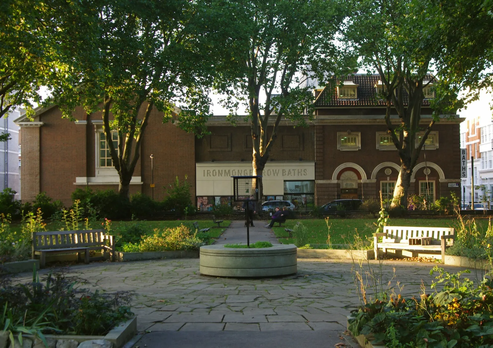 Fachada de ladrillo de los Ironmonger Row Baths vista desde el jardín detrás de la iglesia de St Luke, con árboles y bancas