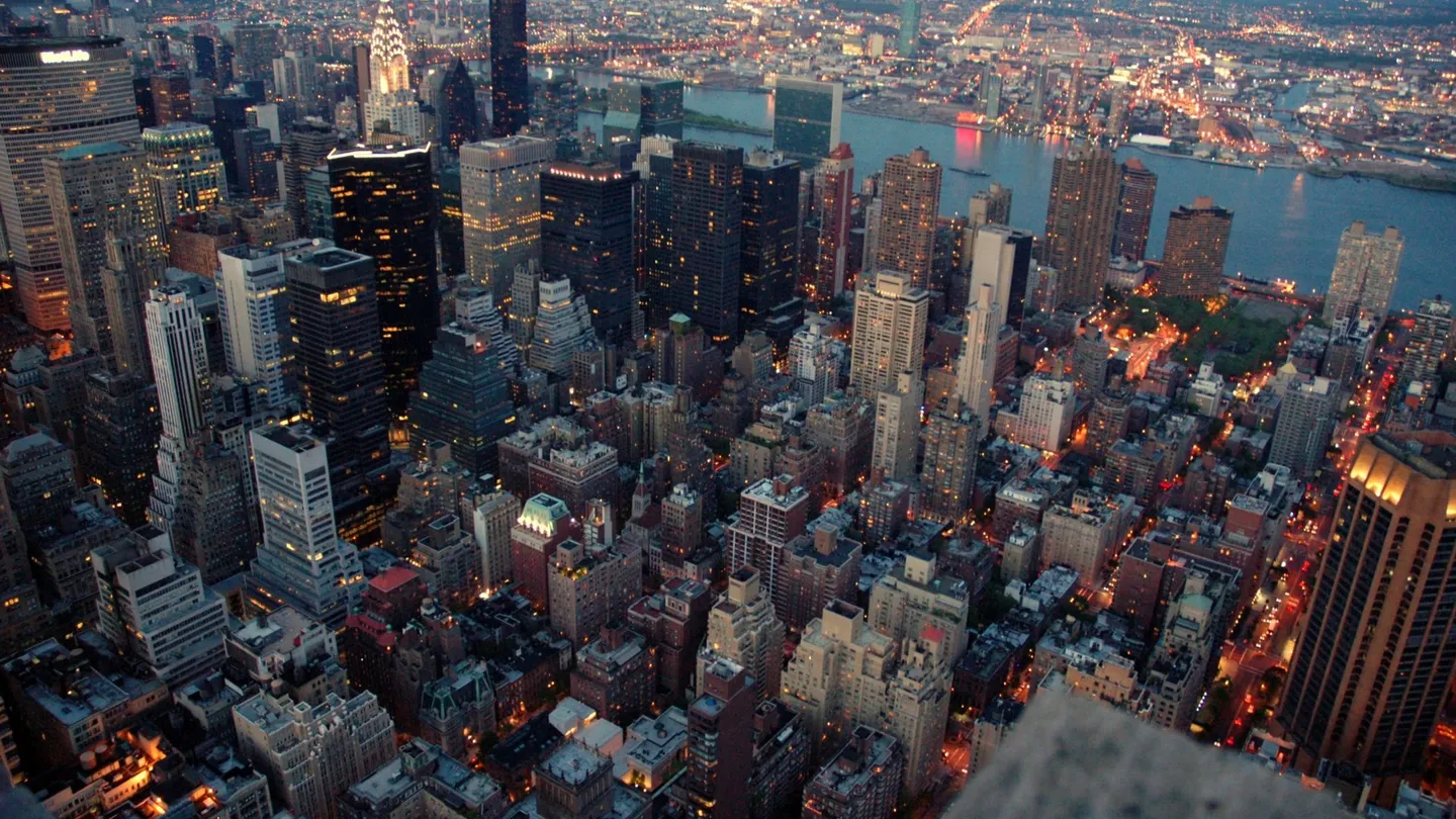 Manhattan vista desde lo alto al atardecer, con los edificios de Midtown iluminados y el East River al fondo