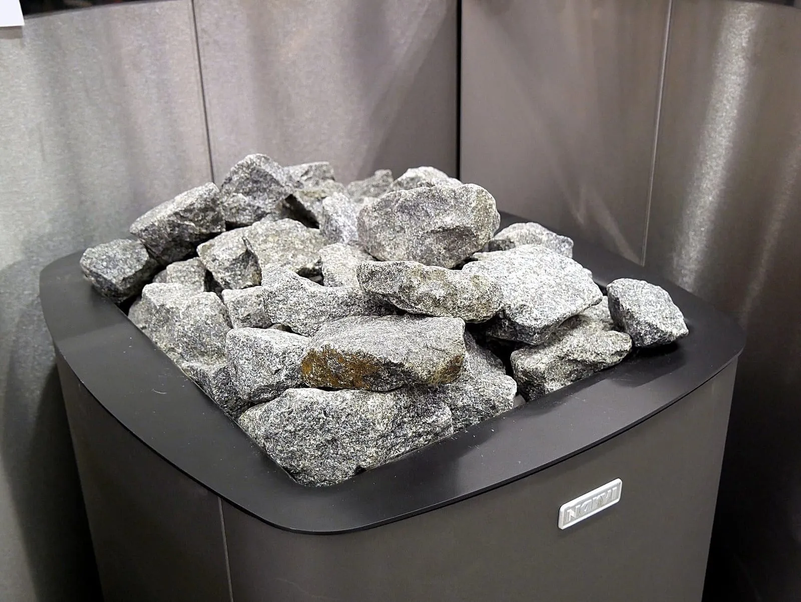 Piedras grises apiladas sobre un calentador de sauna eléctrico de acero