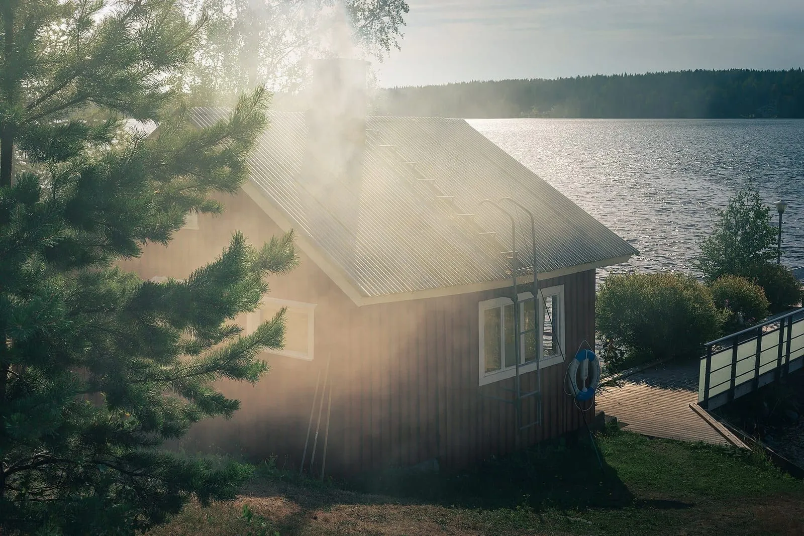 Humo saliendo de la chimenea de un sauna de madera a la orilla de un lago en Finlandia, entre pinos