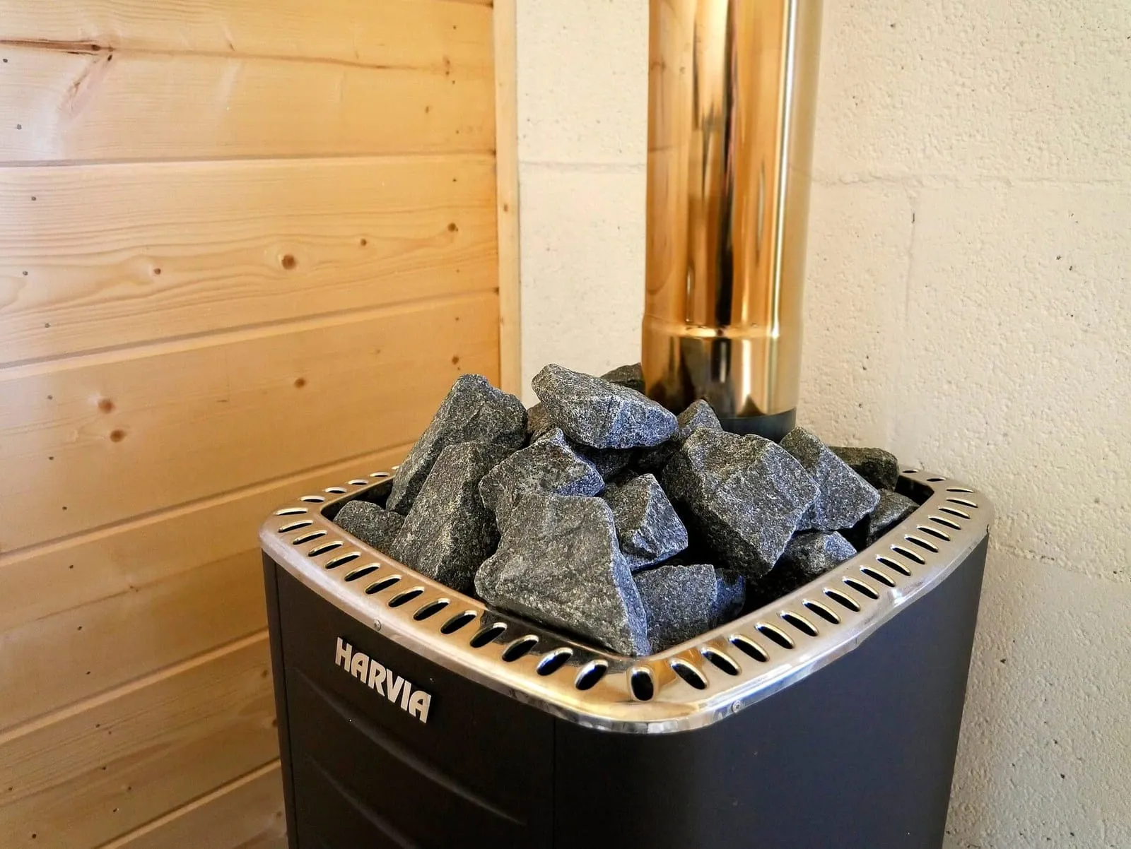 Calentador de sauna eléctrico negro con piedras arriba, en una esquina de sauna de madera clara