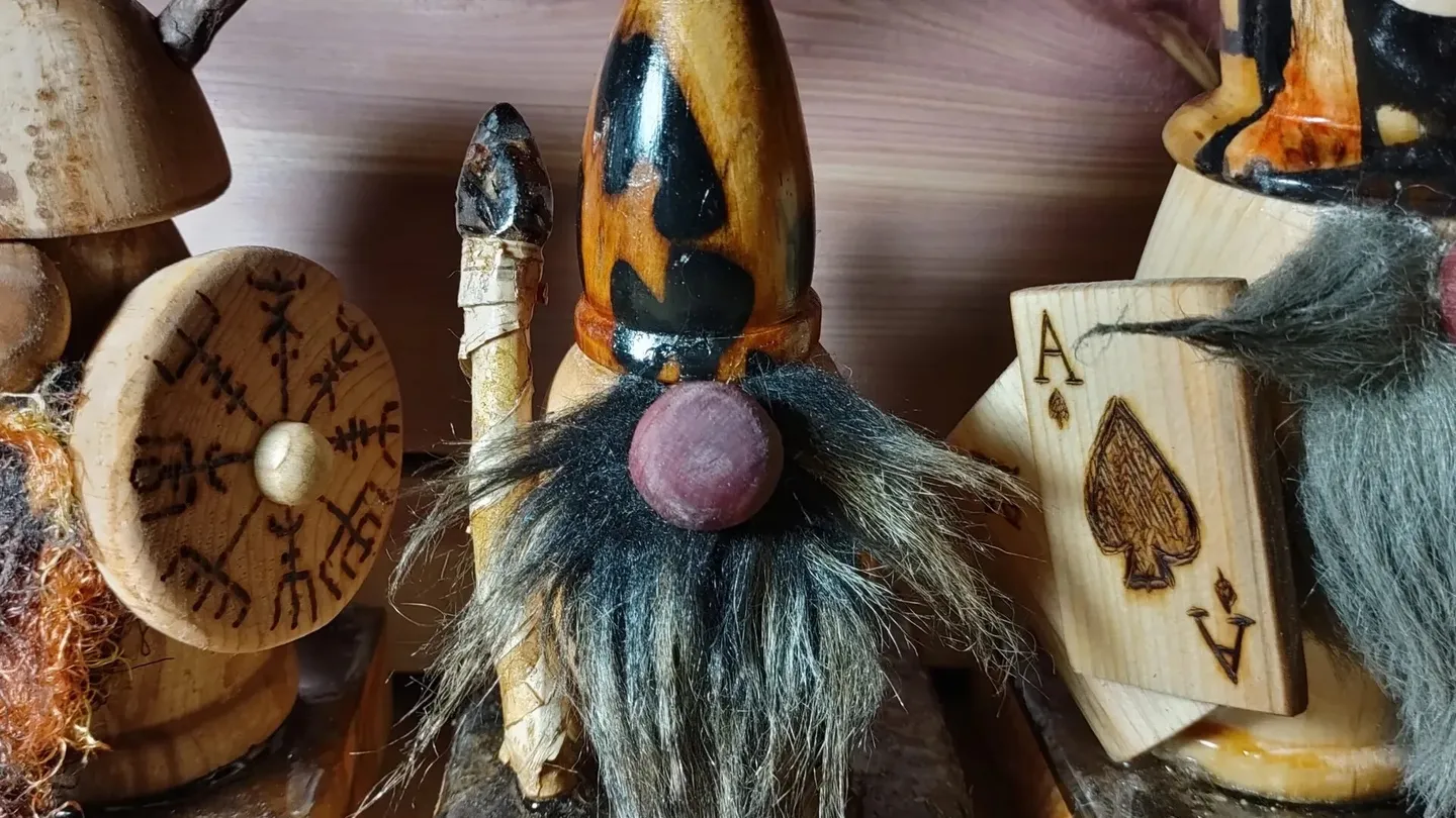 Tres saunatonttu de madera tallada con barbas de pelo en una repisa de madera; el del centro, de gorro puntiagudo y nariz redonda, sostiene un bastón