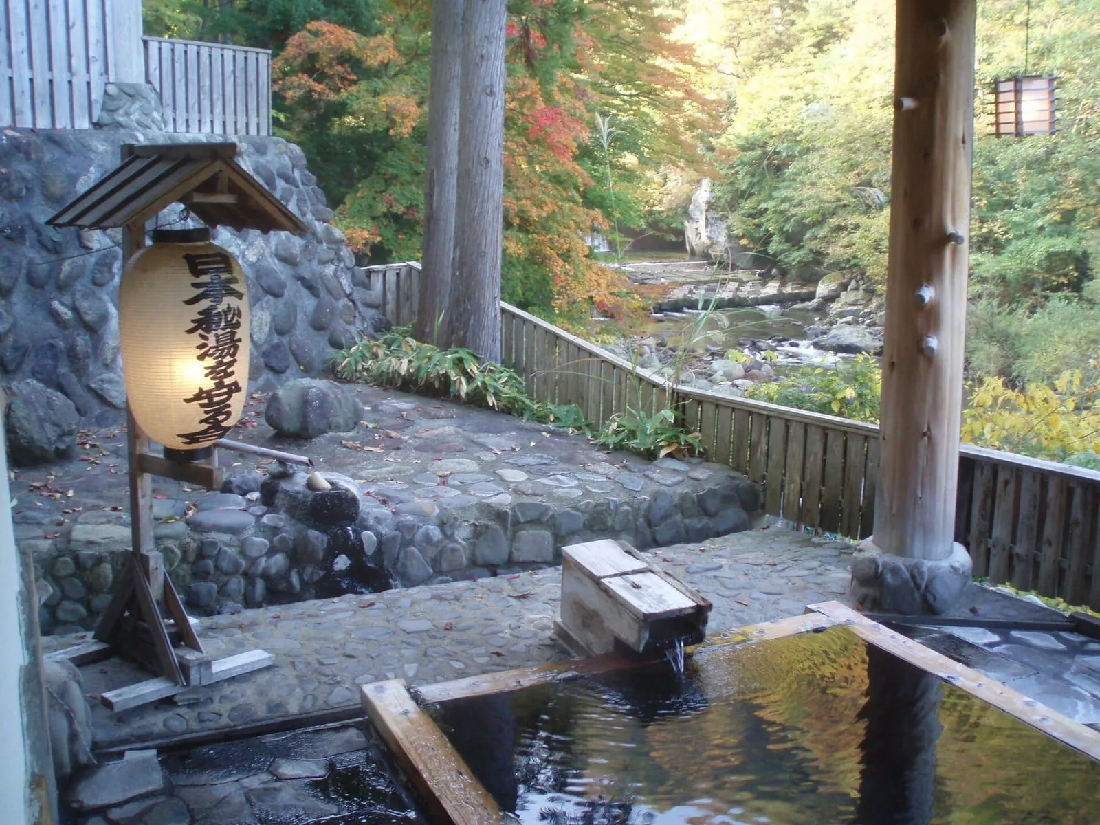Baño de piedra al aire libre en Takanoyu Onsen, Akita, entre árboles y una linterna de madera