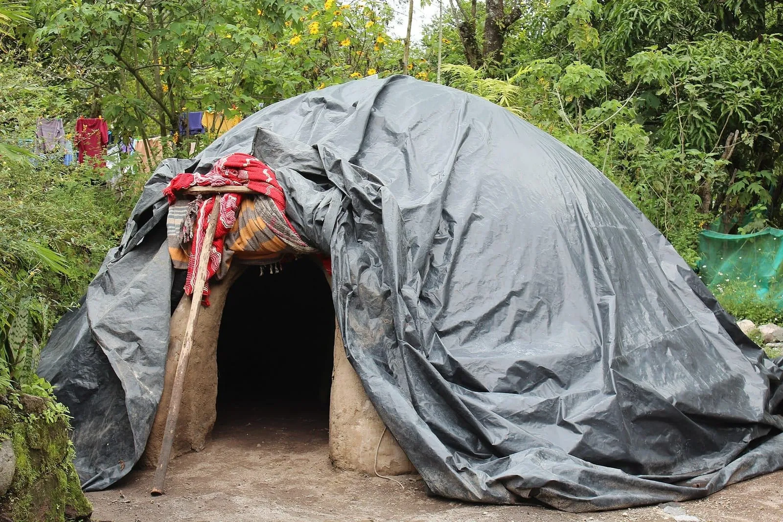 Temazcal en forma de cúpula cubierto con lona oscura, con entrada baja decorada con telas, en Comaltepec