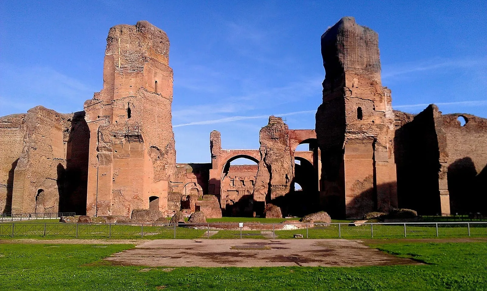 Ruinas de ladrillo de las Termas de Caracalla, en Roma, con muros altos y arcos vistos desde el césped hacia el caldario